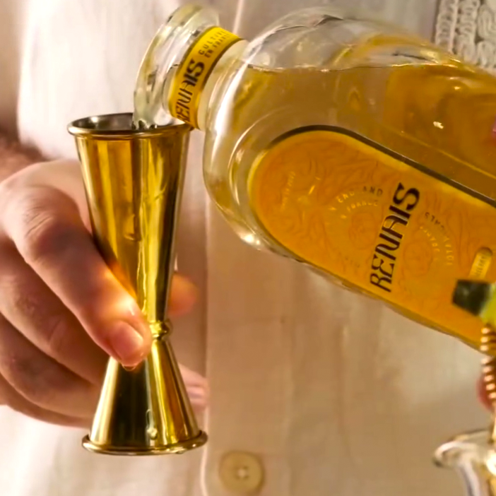 Pouring liquid into a jigger from a yellow-labeled bottle.
