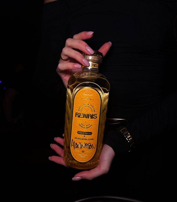 A person holding a Renais gin bottle with a distinctive yellow label.